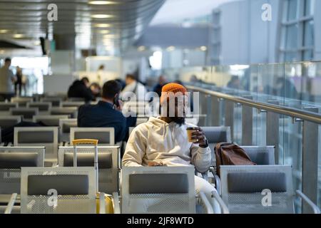 Young African man drinking coffee and eating sandwich while waiting for flying at airport terminal Stock Photo