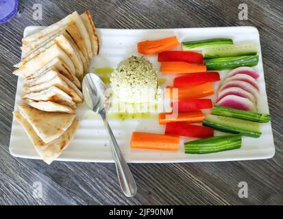 Edamame hummus with pita bread triangles, carrot sticks, cucumbers, and radishes on white serving platter. Stock Photo