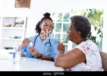African american female doctor giving medicines to senior patient while sitting at table at home Stock Photo