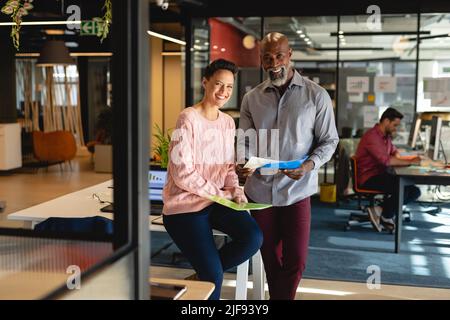 Portrait of smiling multiracial male and female colleagues with file in creative office Stock Photo
