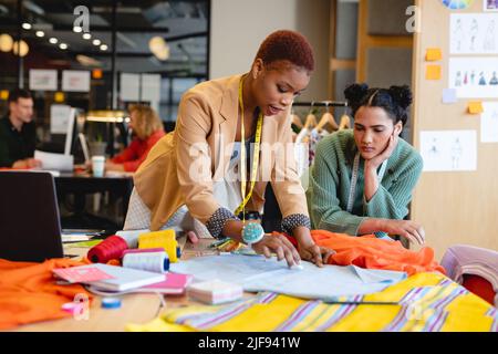 Multiracial young female fashion designers discussing over fabric in creative office Stock Photo