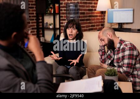 Psychology specialist taking notes on paper at couple therapy with angry partners, talking about relationship issues. Doing psychoanalysis with married people, giving counseling advice. Stock Photo