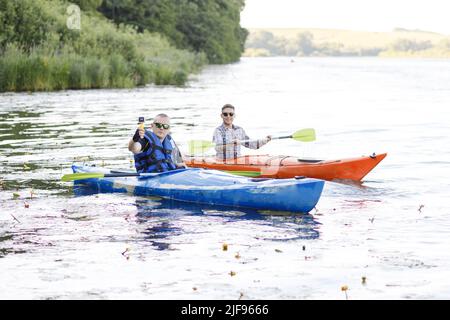 Kayaking on the river. Two young men sit in kayaks and take a selfie with a portable camera. The concept of water entertainment. Stock Photo