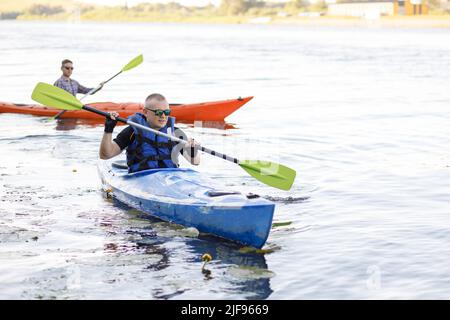 Kayaking on the river. Two young men are sitting in kayaks and rowing on the lake. The concept of water entertainment. Stock Photo
