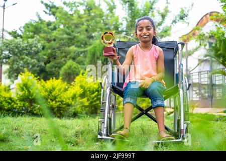 concpe tof inspiration and motivation, showing by young teenager girl kid with disability celebrating by holding trophy on wheelchair Stock Photo