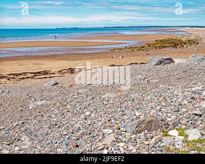 two figures on Dinas Dinlle beach near Caernarfon North Wales with pebbles in the forefround and the Irish Sea in the background Stock Photo