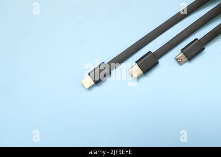 Smartphone or mobile phone standard charging cable plugs flat lay. Micro USB, type c and lightning cable in blue background with copy space. Stock Photo