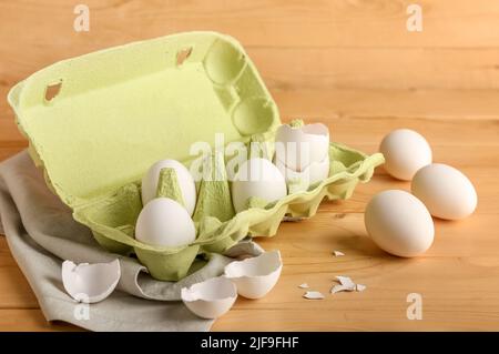 Cardboard holder with white chicken eggs and shells on wooden background Stock Photo