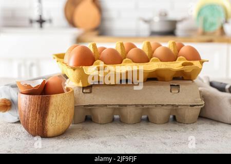Holders with chicken eggs and bowl of shells on table in kitchen Stock Photo