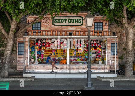 Two men talking in the shade at a colourful shooting gallery on a hot summer afternoon in Siracusa, Sicily, Italy Stock Photo