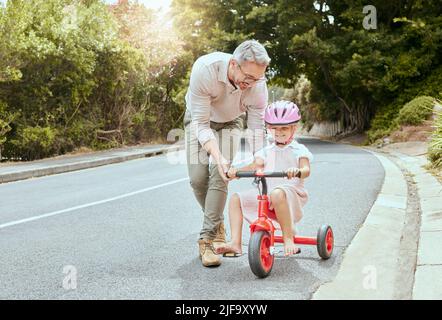 A happy father teaching his little girl to ride a bike outside. Cute Caucasian child wearing a pink helmet and cycling while bonding with her dad Stock Photo