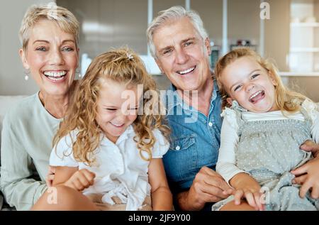 A happy caucasian mature couple bonding with their adopted kids in the living room. Two sisters relaxing with their grandparents while taking selfies Stock Photo