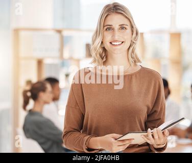 Portrait of a confident young caucasian businesswoman holding notebook planner in an office with her colleagues in the background. Ambitious Stock Photo