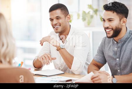 Young mixed race businessman speaking and listening to colleagues during a meeting in an office boardroom. Staff sharing feedback and explaining ideas Stock Photo