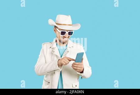 Happy man in hat, sunglasses and leather jacket sending messages on mobile phone Stock Photo