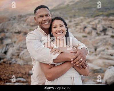 Closeup portrait of an young affectionate mixed race couple standing on the beach and smiling during sunset outdoors. Hispanic couple showing love and Stock Photo