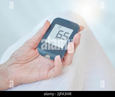 Closeup of a senior diabetic woman checking her blood sugar glucose levels with a diabetes reading strips machine. One unknown elderly woman doing a Stock Photo