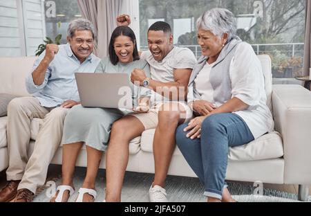 Happy and affectionate mixed race family of four using a laptop to watch sports and cheer on their favourite team in the home living room. Married Stock Photo