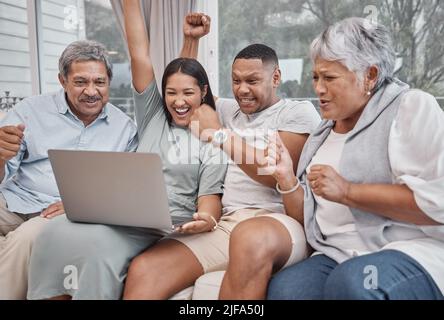 Happy and affectionate mixed race family of four using a laptop to watch sports and cheer on their favourite team in the home living room. Married Stock Photo