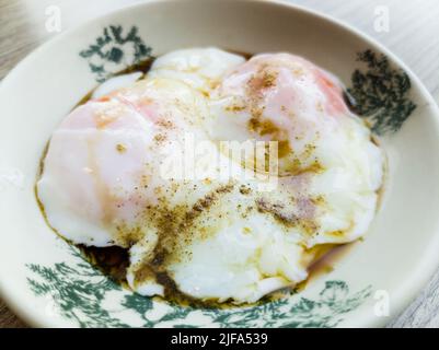 Close-up view two half boiled eggs served with soy sauce and white pepper. Stock Photo
