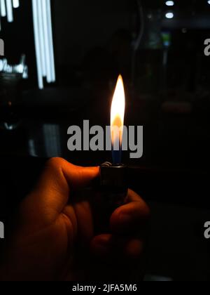 A Human hand igniting a lighter with dark background Stock Photo