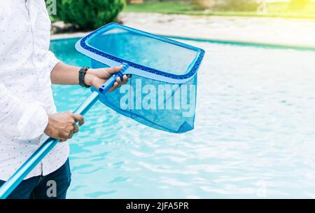 Hands holding a skimmer with blue pool in the background. A man cleaning pool with leaf skimmer. Man cleaning the pool with the Skimmer, Person with Stock Photo