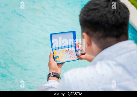 Person holding complete water test kit with blurred pool background, Hand holding Water Test Kit on blurred pool background, Hand holding a pool ph Stock Photo