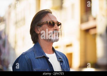 Mature man walking in street, looking at urban city enjoying free time. Handsome middle aged man waiting on his wife or lady to date standing at old town. Traveling mature man in old town.  Stock Photo