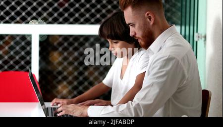 Candid parent and child together in front of computer doing homework at night. Dad helping son to learn Stock Photo