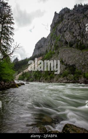 Flowing water next to old green railway bridge over wild river Enns in cloudy weather in Gesause National Park near town of Admont in centre Austria. Stock Photo