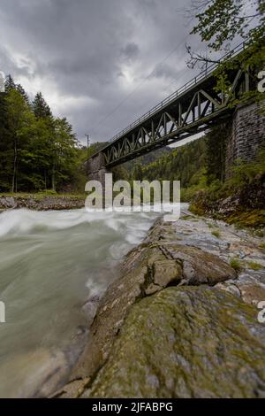 Old green railway bridge over wild river Enns in cloudy weather in Gesause National Park near town of Admont in centre Austria. Long exposure photo wi Stock Photo