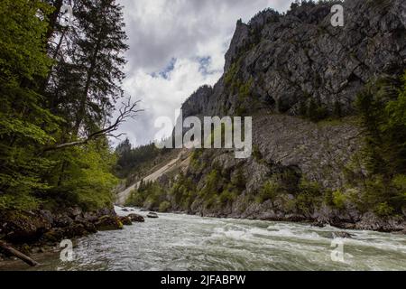 Flowing water next to old green railway bridge over wild river Enns in cloudy weather in Gesause National Park near town of Admont in centre Austria. Stock Photo