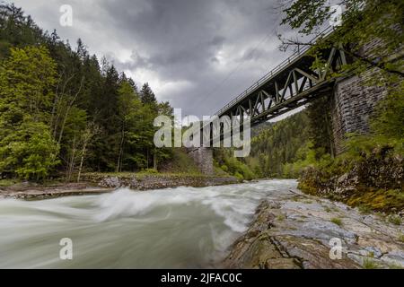 Old green railway bridge over wild river Enns in cloudy weather in Gesause National Park near town of Admont in centre Austria. Long exposure photo wi Stock Photo