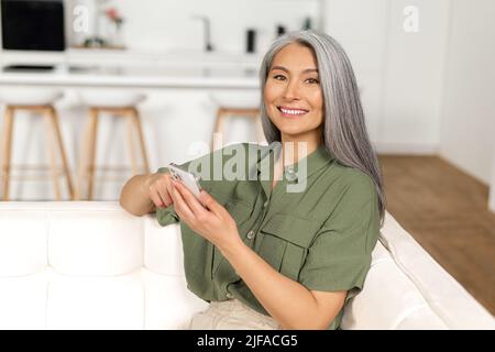 Contemporary senior woman spends time with a smartphone, mature woman scrolling news feed on the mobile phone, texting online with friends or children, enjoying messaging in social networks Stock Photo