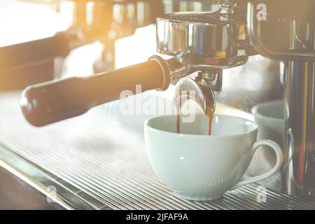 Close up coffee extraction from coffee machine to white cup in coffee shop. Food and beverage concept Stock Photo