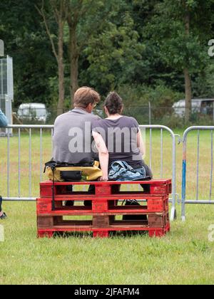 Hulst, Netherlands, June 26, 2022, couple sitting side by side on red stacked wooden pallets Stock Photo