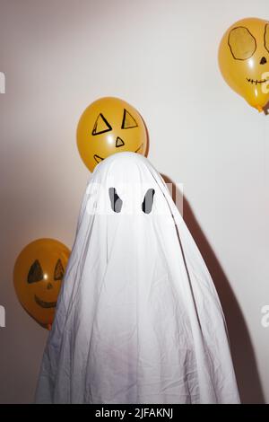 Happy Halloween. Man in a white ghost suit and painted orange balls. Different emotions of joy, anger, laughter. Festive design, party concept. Stock Photo