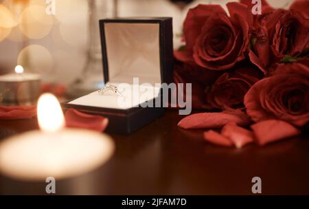Closeup of romantic engagement ring box, fresh red roses and candles in an empty room at night. Getting ready and prepared for surprise proposal Stock Photo