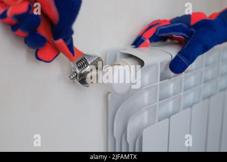 Plumber changes or adjusts radiators. Male gloved hand holding apipe wrench Stock Photo