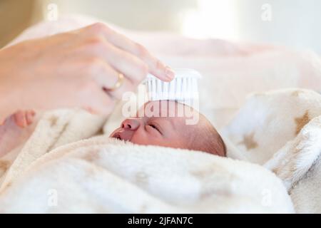 hands of a mother carefully combing the hair of her newborn baby wrapped in a soft blanket after washing him and changing his diaper. health care and Stock Photo