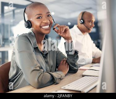 Portrait of happy young african american call centre telemarketing agent talking on a headset while working on a computer in an office. Confident Stock Photo