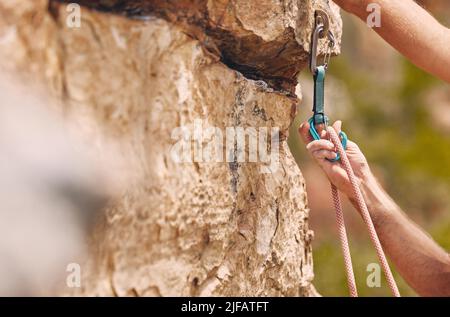 Closeup shot of an unrecognizable man using a carabiner while mountain climbing. Unknown male checking his safety equipment while adjusting his rope Stock Photo
