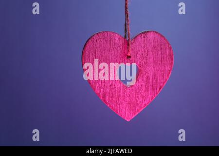 Pink wooden heart suspended by string against a dark blue-purple background Stock Photo