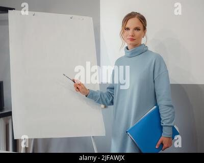 Young female trainer or speaker making whiteboard presentation for employees in office, focused woman trainer presenting business project on flipchart at meeting. mock-up Stock Photo