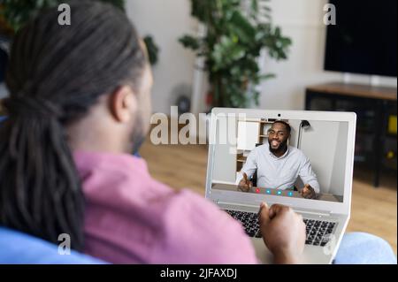 Two male African-American male friends using computer app for video meeting, talking online, has virtual discussing. Black man holding video call on the laptop, back view Stock Photo