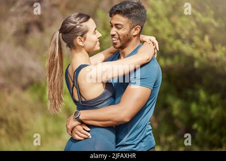 Affectionate young interracial couple taking a break from exercise and run outdoors. Loving man and woman hugging while motivating each other towards Stock Photo