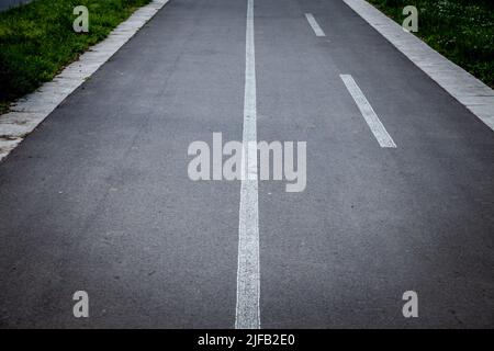 Picture of a bicycle lane with the focus on the white road markings, white lines, indicating the pathway is dedicated to bicycles and pedestrians. Stock Photo