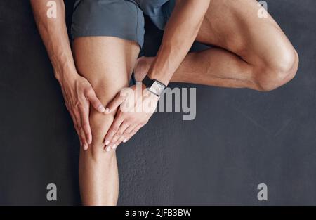 Closeup of one mixed race man from above holding his sore knee while exercising in a gym. Guy suffering with painful leg injury from fractured joint Stock Photo