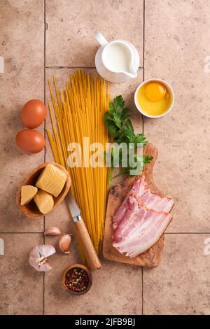 Ingredients for Pasta Carbonara. Traidtional Italian Pasta Carbonara Ingredients bacon, spaghetti, parmesan and egg yolk, garlic. Beige old tile table Stock Photo