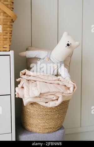A stuffed toy is a homemade teddy bear on a basket with laundry in the decor of a children's room in a Scandinavian or minimalist style Stock Photo